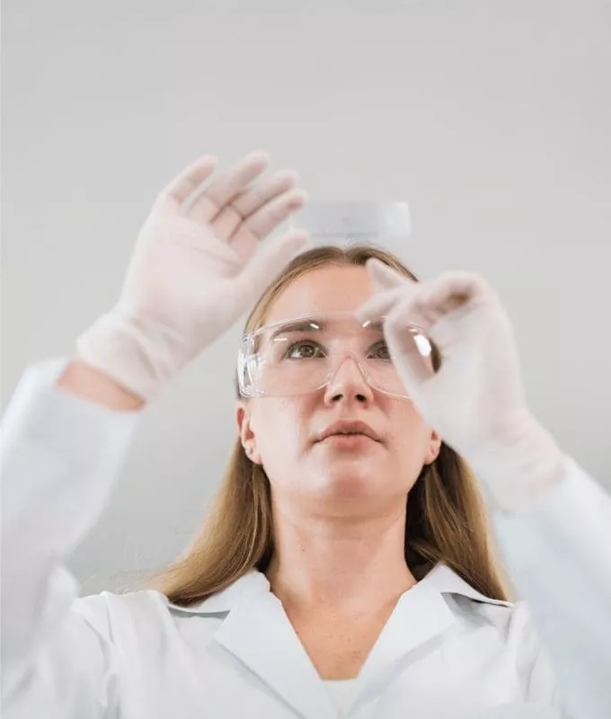 Female scientist wearing safety glasses and gloves inspecting a microscope slide in a laboratory.